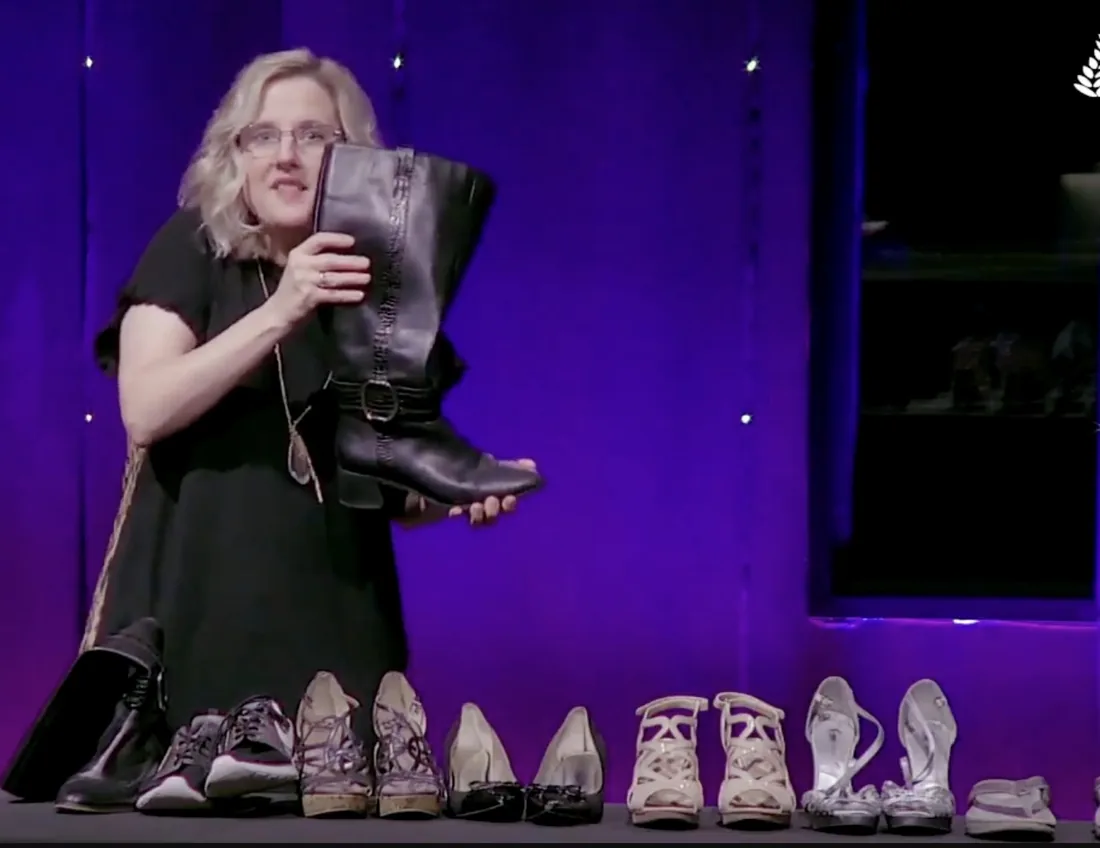 Kim Gilson preaching with a row of shoes laid out across the stage